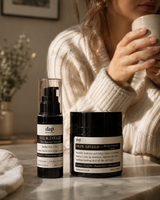 Two skincare products on a table with a person holding a mug in the background