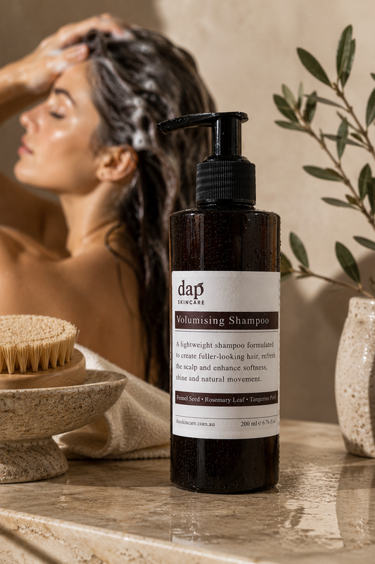 Woman washing her hair with a bottle of Dap Volumising Shampoo on a wooden surface.