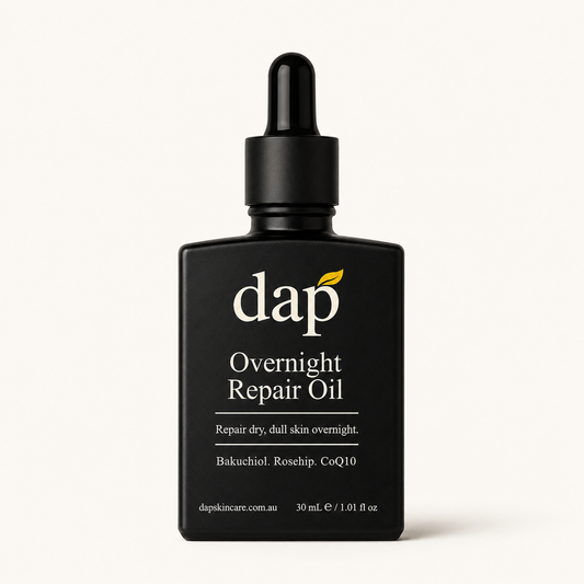 A black dropper bottle of DAP Overnight Repair Oil on a clean, light off-white background. The label features white text and a small yellow leaf accent under the DAP logo.