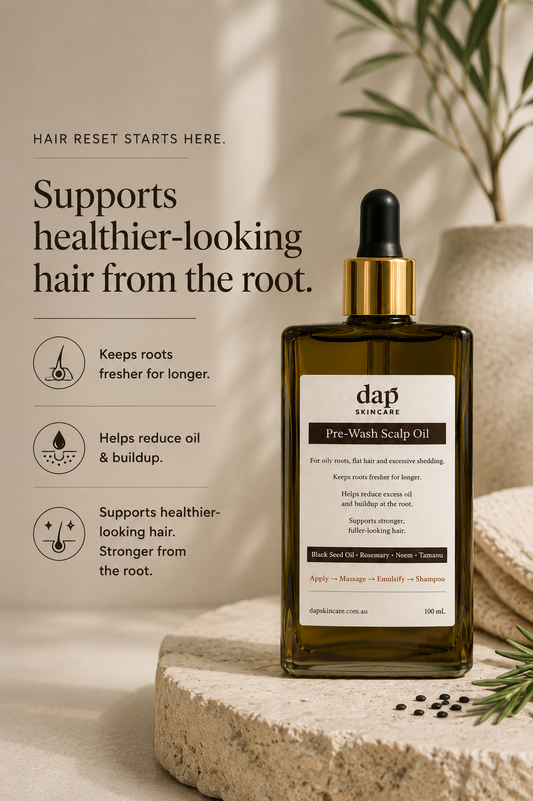 A bottle of dap skincare Pre-Wash Scalp Oil stands on a stone slab in a styled setting with text callouts on the left. The bottle is dark amber glass with a black dropper cap and a gold collar, and the label is white with black text.
